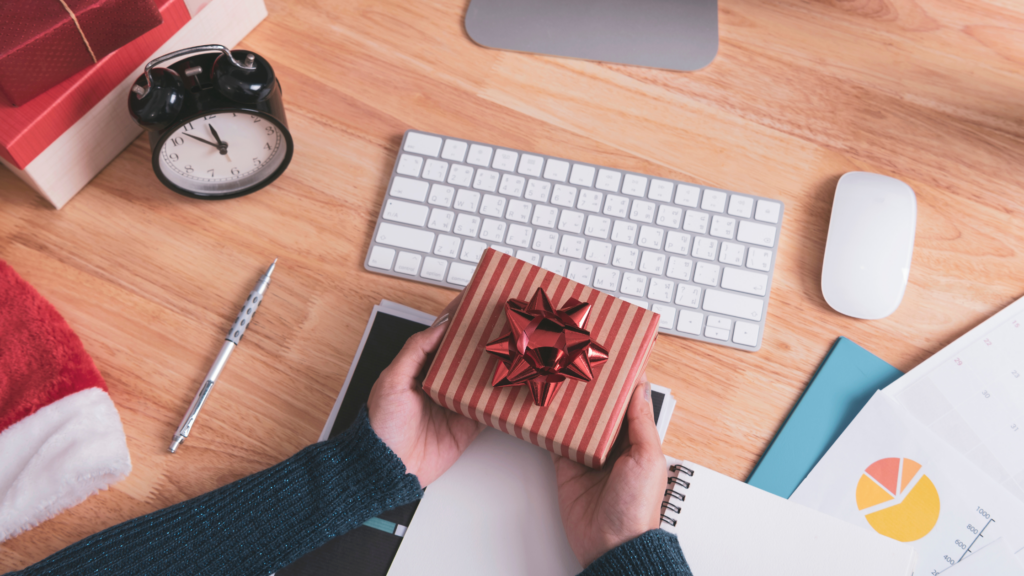 Image of a desk with work items and documents and an employee golding an employee gift