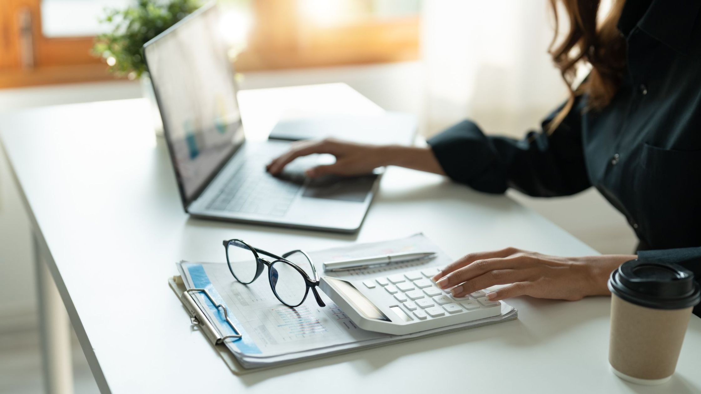 Image of a female at her desk working on household budgets and managing finances with a laptop and calculator