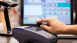 A retailer cashier topping up a SWIRL Prepaid Mastercard by swiping the card via Payzone for a customer in their shop